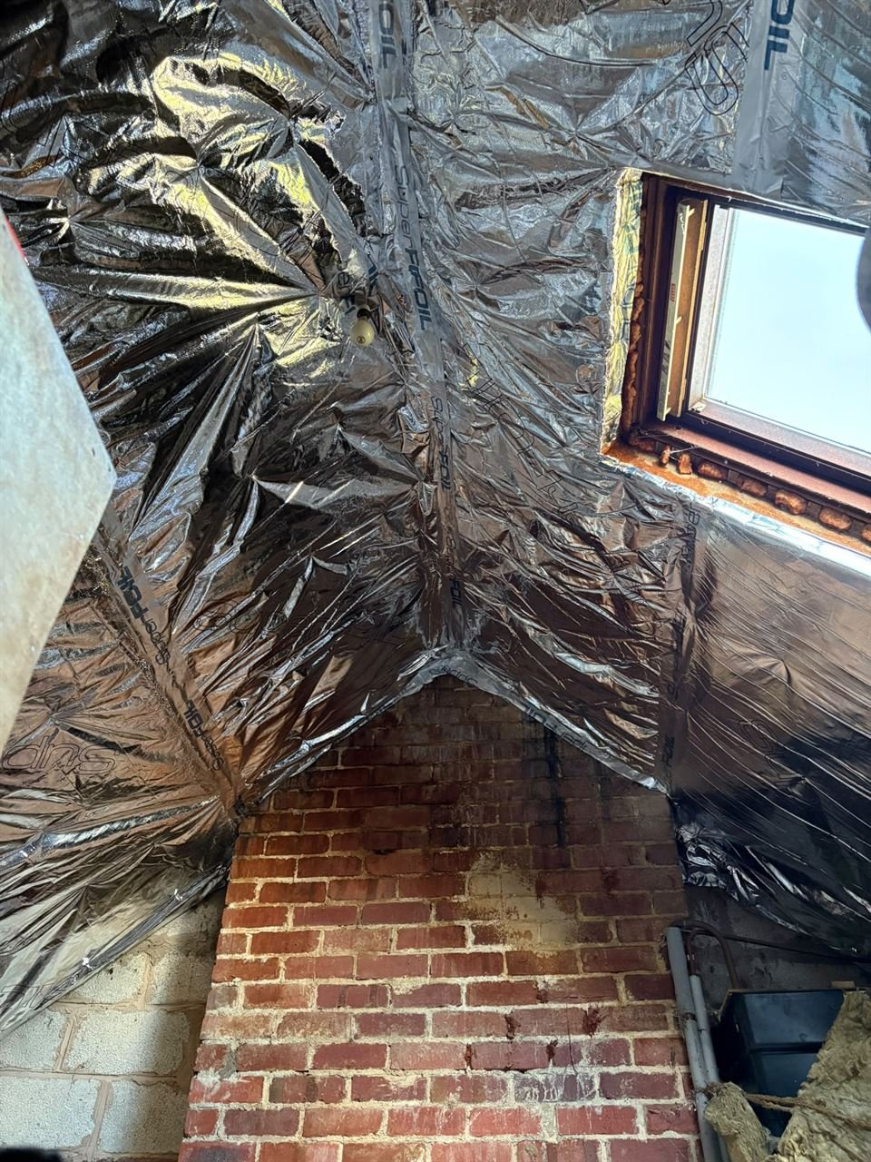 SuperFOIL insulation lining the sloping roof around a roof window, seen from beside a brick gable wall